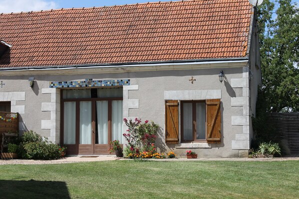 A two-story building with a tiled roof, a front entrance with a wooden door, and a small garden area with potted plants and flowers. - Lodging near Amboise, Chenonceau, Chaumont / Loire  (Mosnes)