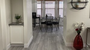 Un coin repas comprenant une table et des chaises, un vase avec des fleurs et une étagère fixée au mur.