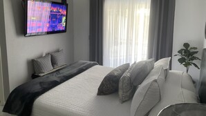 Une chambre à coucher moderne avec un lit, un téléviseur fixé au mur et une fenêtre avec des rideaux.