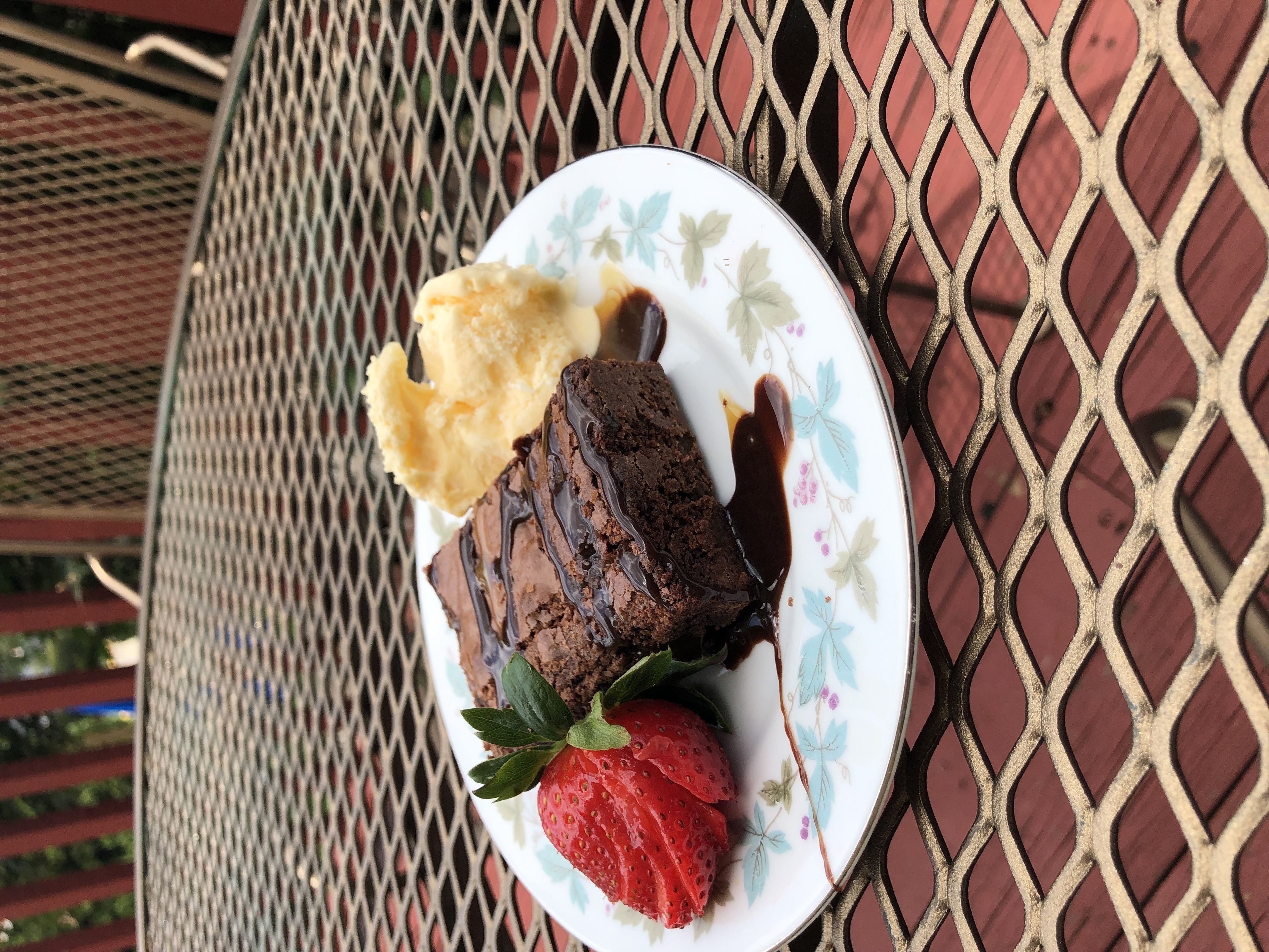 A plate with a dessert consisting of a chocolate cake, a scoop of vanilla ice cream, and a strawberry on a decorative plate.