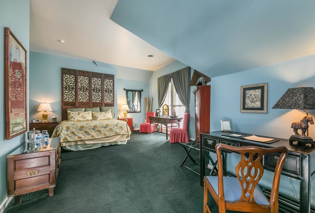 A hotel room with a bed, desk, chair, and a desk lamp.