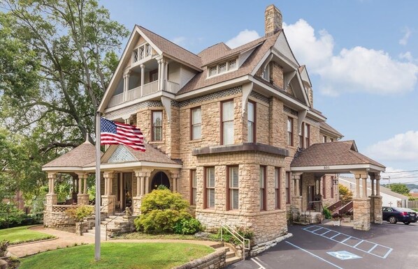A stone building with a gabled roof, a flagpole with an American flag, and a parking lot. - The Mayors Mansion Inn (Chattanooga)
