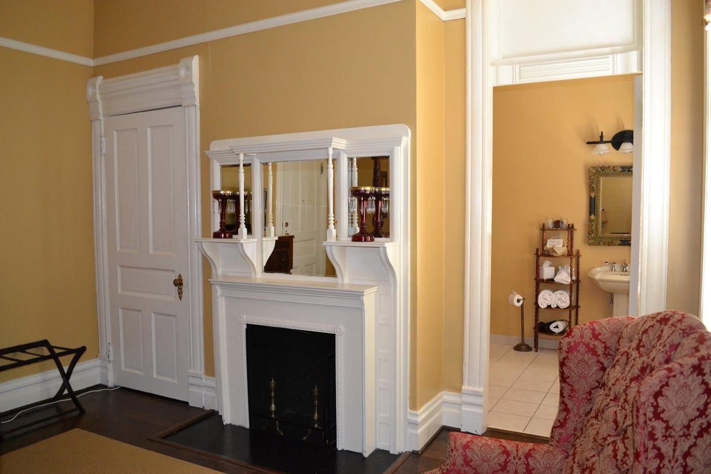 A room with a white fireplace, a mirror above it, and a patterned armchair.