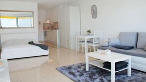 Un salon moderne et bien éclairé, avec un canapé, une table à manger et des chaises, une table basse blanche et un grand miroir au mur.