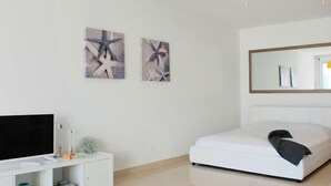 Une chambre moderne comprenant un lit, un téléviseur, une armoire et deux œuvres d’art abstraites accrochées au mur.