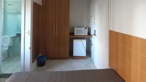 A small, compact room with a bed, a wooden wardrobe, a microwave, and a small refrigerator. - Thermas Place - Férias em Caldas Novas (Caldas Novas)