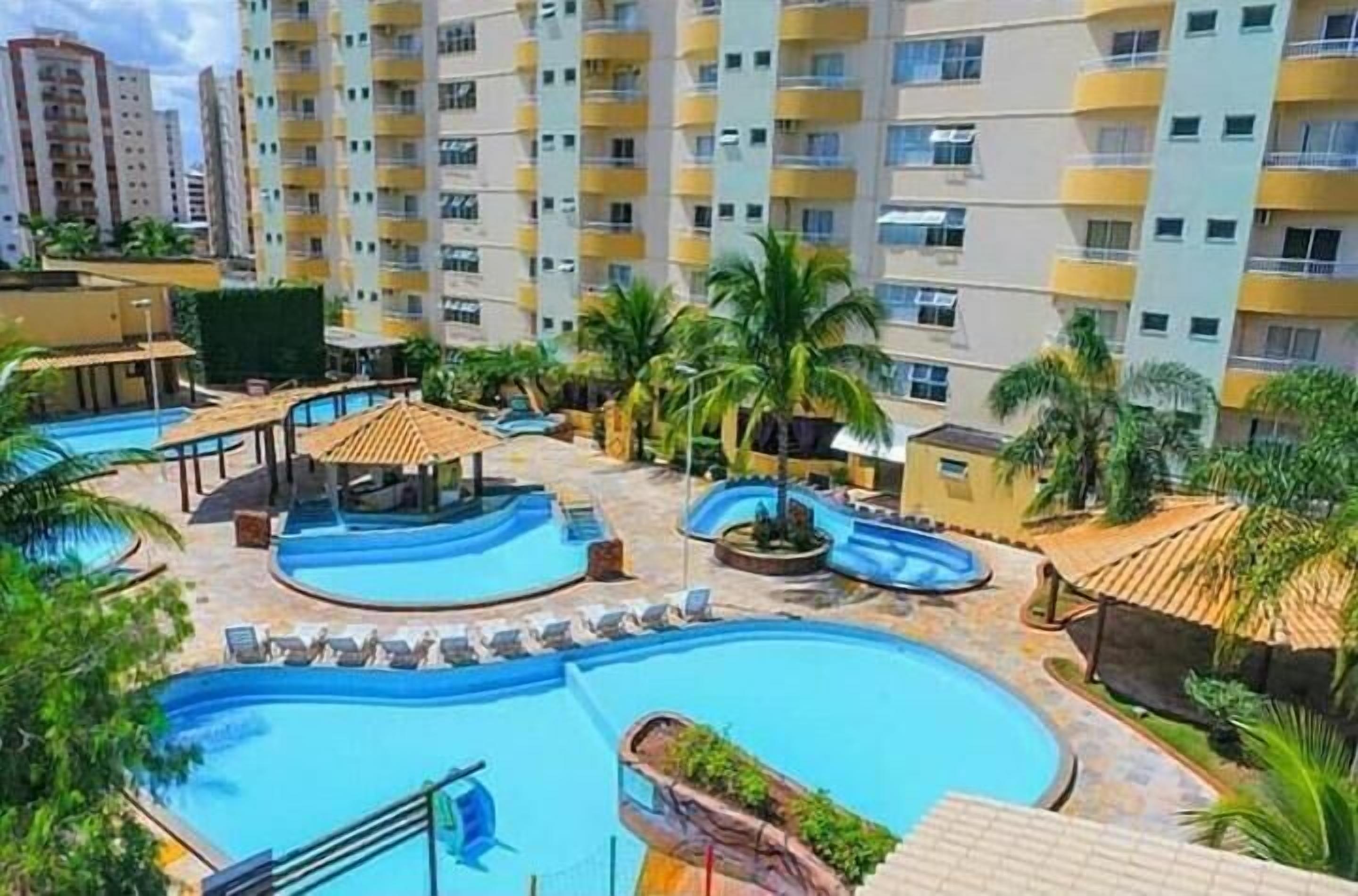 A hotel with a swimming pool, palm trees, and a view of high-rise buildings.