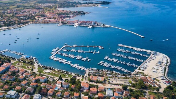 En vy från ovan över en småbåtshamn med många båtar förtöjda, omgiven av bostadshus och en stor vattenyta.