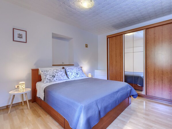A bedroom with a wooden bed, a small bedside table, a nightstand, a mirror, and a wardrobe. - Apartment Bumbak by Interhome (Umag)