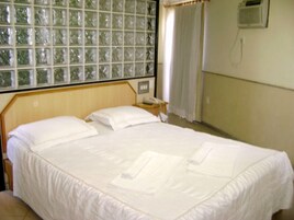 A room with a large bed, a bedside table, a telephone, and a window with curtains.