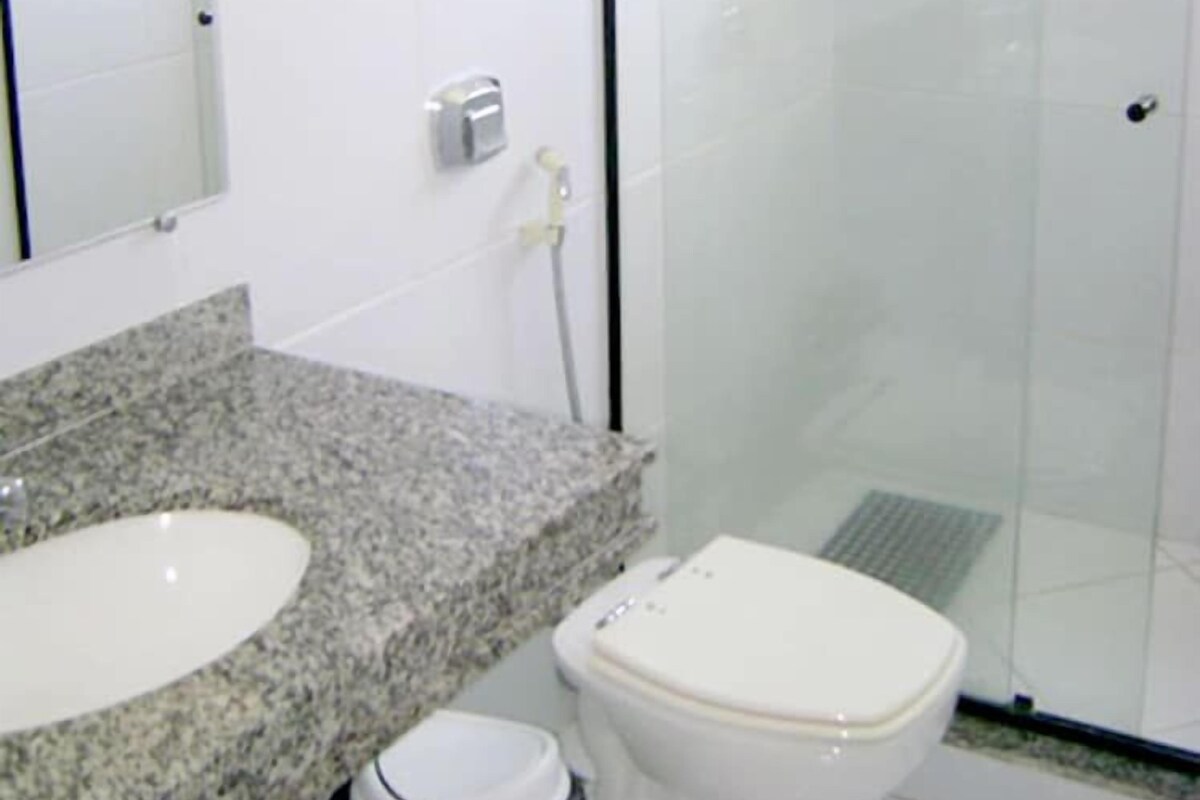 A bathroom with a granite countertop sink, a toilet, and a glass-enclosed shower stall.