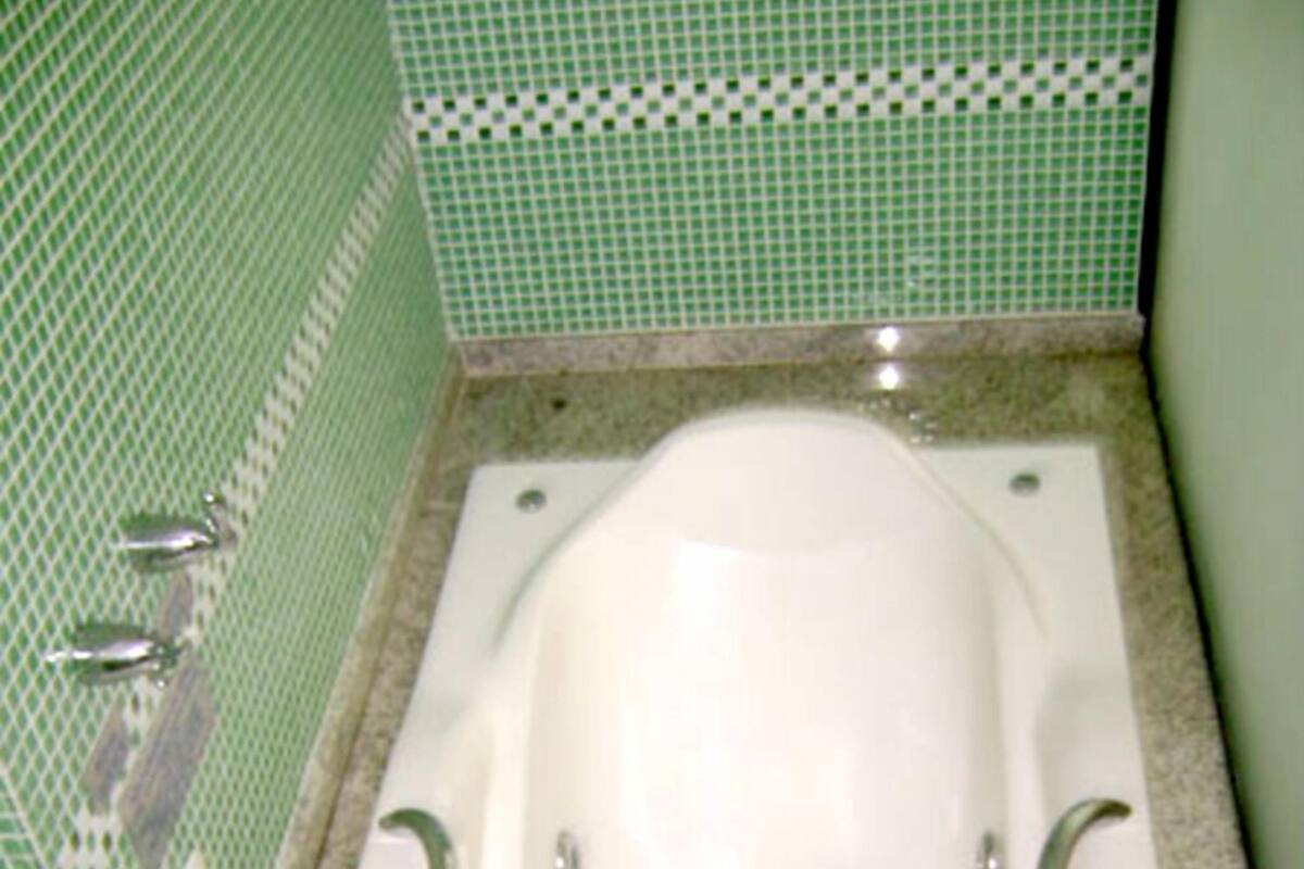 Une baignoire blanche dans une salle de bain aux murs recouverts de carreaux verts et dotée d’un comptoir en granit.