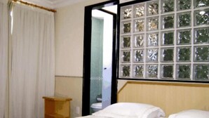 A hotel room with a bed, a small wooden nightstand, and a window with a view of greenery.
