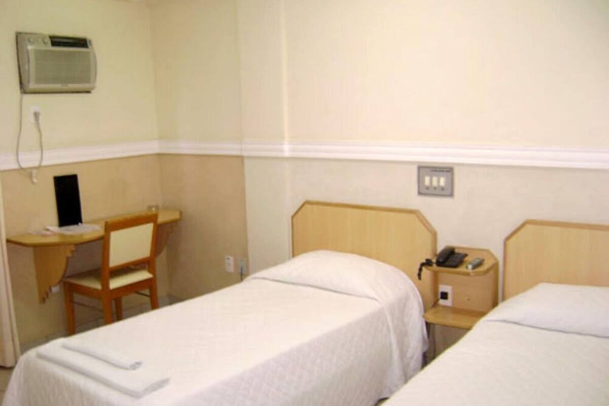 Une chambre d’hôtel avec deux lits simples, un bureau avec une chaise, un téléphone et un appareil de climatisation.