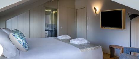 Habitación de hotel moderna con una cama grande, un pequeño área de descanso, televisión y un baño visible a través de una puerta abierta.