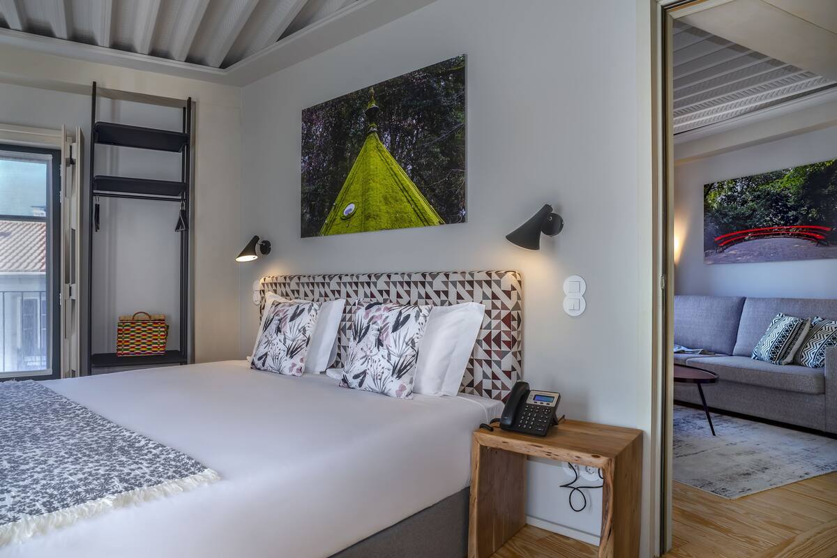 A bedroom with a bed, a bedside table with a phone, a wall-mounted shelf, and a painting.