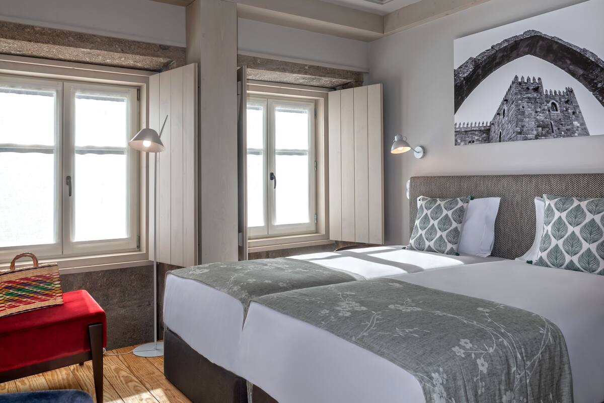 A bedroom with two beds, a red bench, and a wall-mounted lamp.