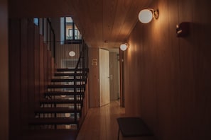 A wooden interior with a staircase, a bench, and wall-mounted lights.