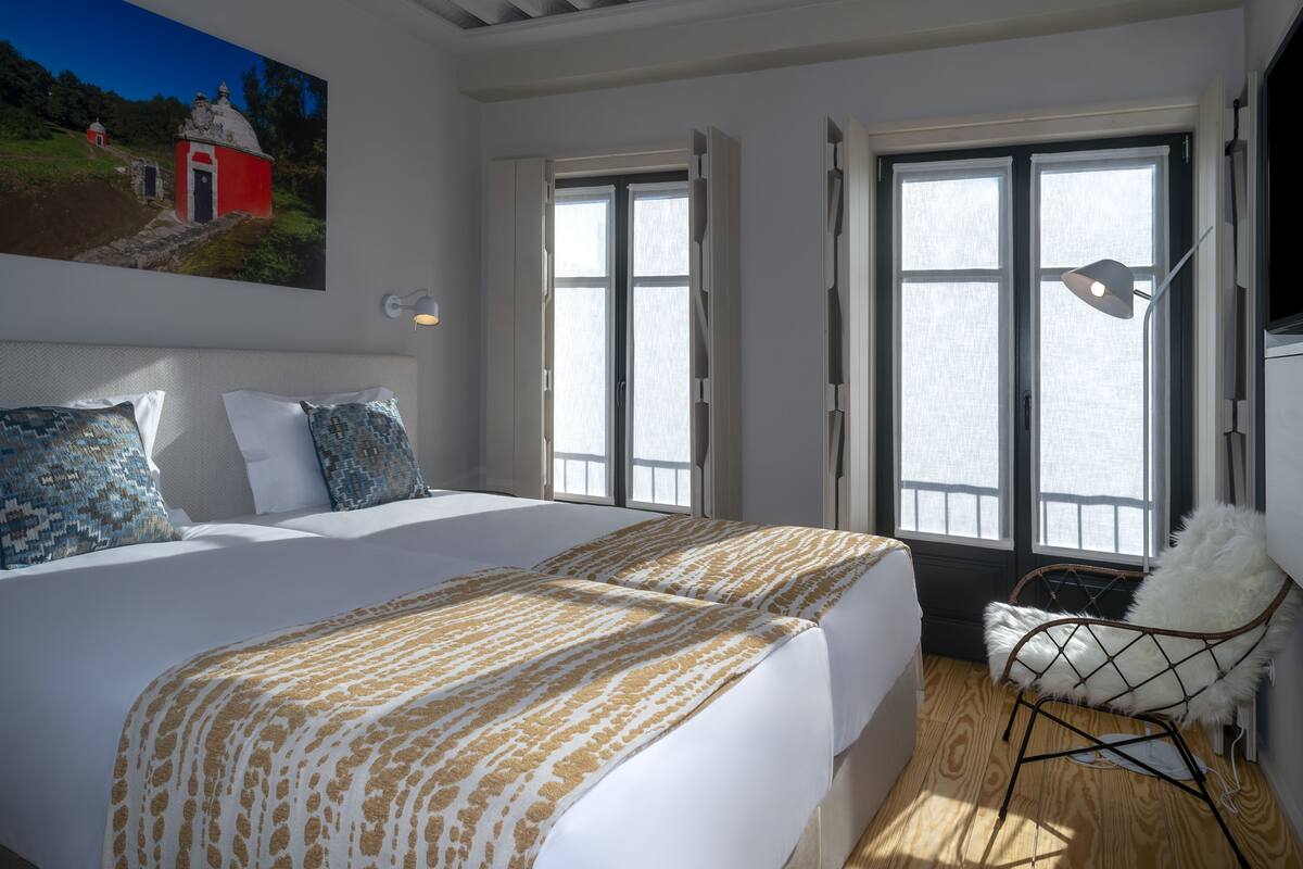 A bedroom with a large bed, a chair, and a window with a view of a red building.