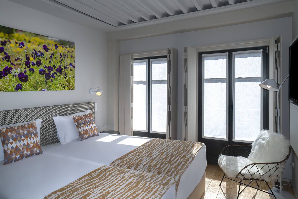 A bedroom with a large bed, two windows, a wall-mounted TV, and a painting of flowers.