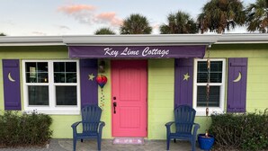 A cottage with a purple awning labeled "Key Lime Cottage," a red door, and two blue Adirondack chairs outside.