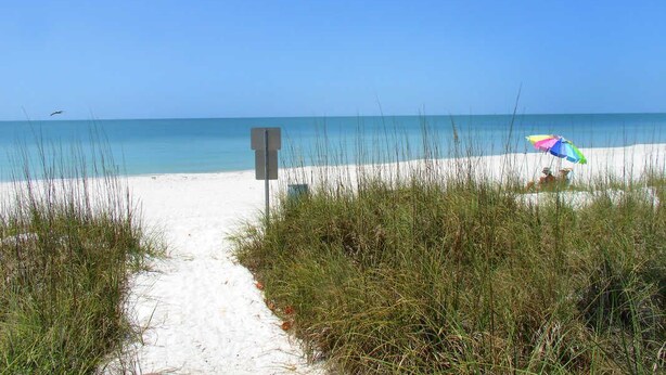 A sandy beach path leading to the ocean with a colorful umbrella and a signpost.