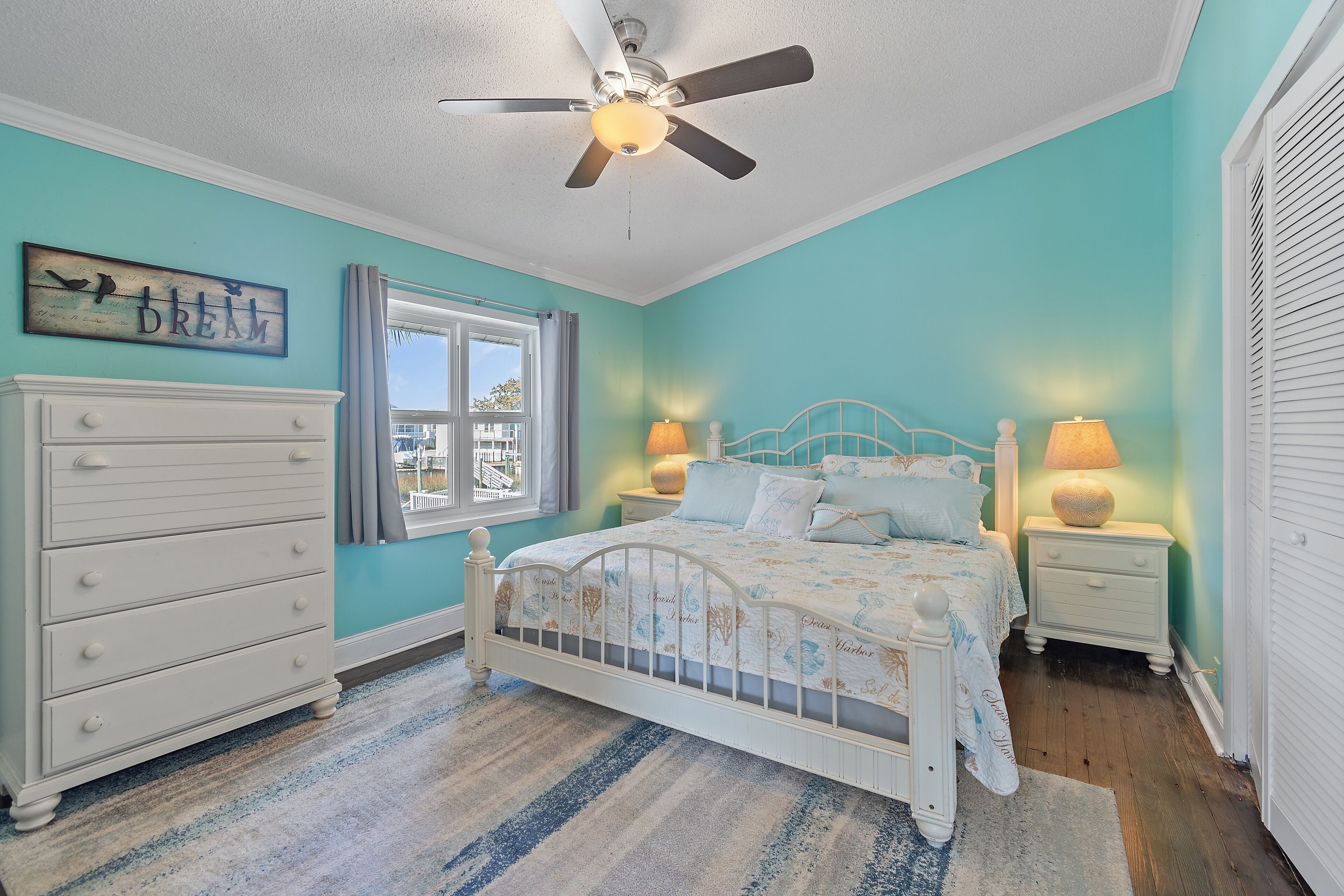 A bedroom with a bed, dresser, ceiling fan, window, and two bedside lamps.