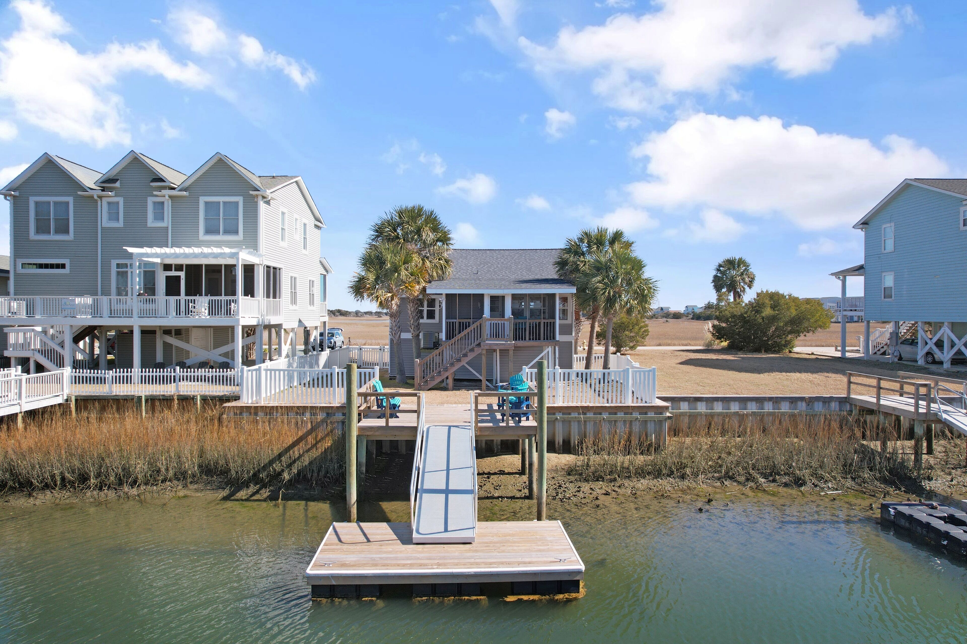 A waterfront property with a dock, a covered deck, and a large house with multiple windows and balconies.