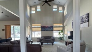 A spacious living room with a high ceiling, large windows, and a ceiling fan. - Mountain Retreat - Close to NAU & Snowbowl (Bellemont)