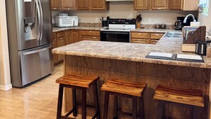 A modern kitchen with wooden cabinets, stainless steel appliances, a granite countertop, and two wooden stools. - Mountain Retreat - Close to NAU & Snowbowl (Bellemont)