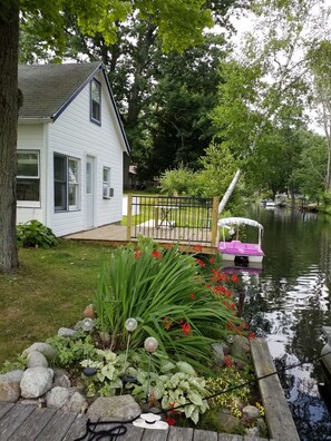 Una casa con terraza que da a un río tranquilo, rodeada de abundante vegetación y un pequeño muelle con un bote.