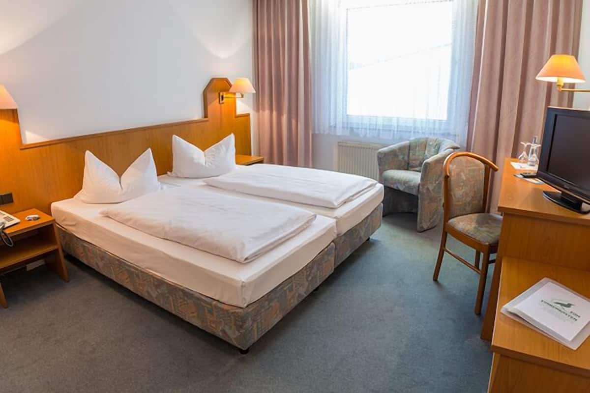 A hotel room with two beds, a desk with a computer, a chair, and a TV.