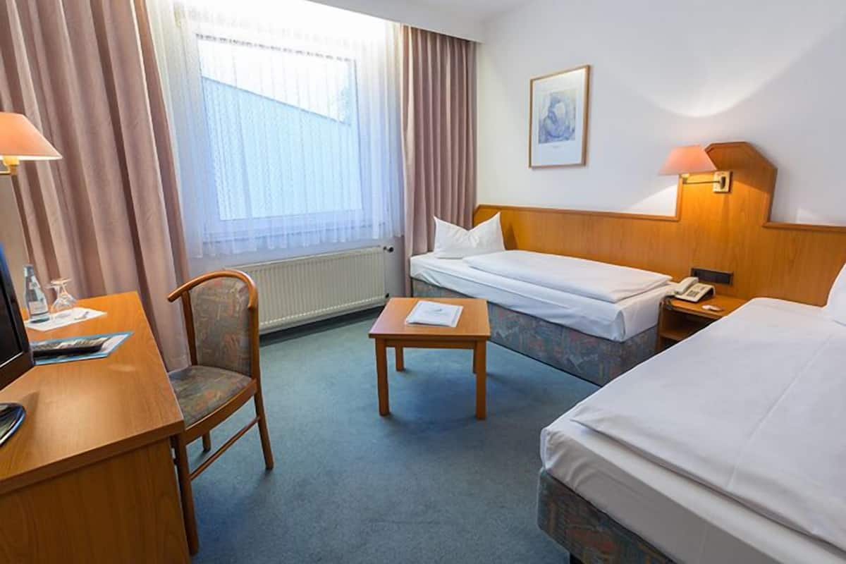 A hotel room with a bed, a desk, a chair, a small table, and a window with curtains.