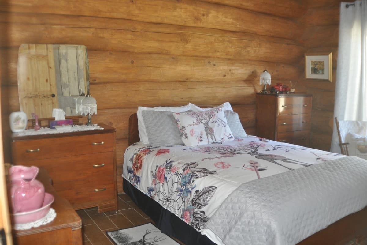 A wooden cabin bedroom with a bed, dresser, and nightstand.