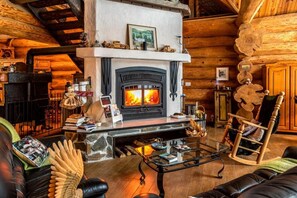 Interior acogedor de una cabaña de troncos con chimenea, mobiliario de cuero y decoración rústica.