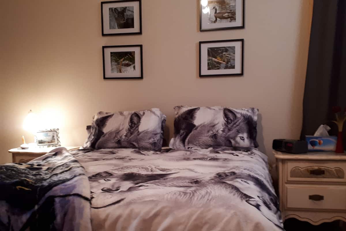 A bedroom with a bed, two framed pictures on the wall, a bedside table, and a nightstand.
