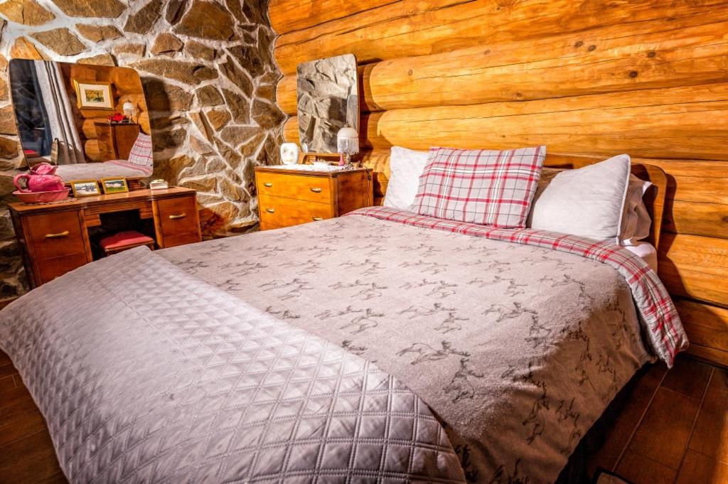 A room with a stone wall, wooden headboard, a bed with a quilted bedspread, a nightstand with a lamp, and a dresser with drawers.