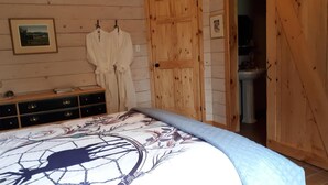 A bedroom with a bed, wooden walls, a dresser, and a door leading to a bathroom. - Au domaine de La Giroux-ette (La Patrie)