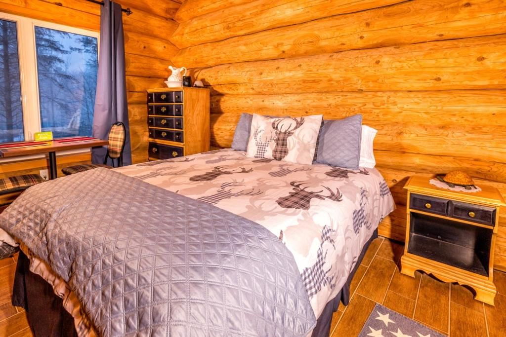A log cabin bedroom with a bed, dresser, and a window with a view of trees.