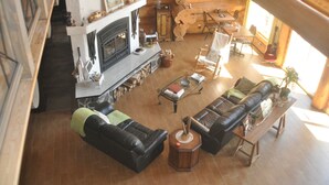 A log cabin interior with a fireplace, leather sofas, wooden dining table, and a staircase. - Au domaine de La Giroux-ette (La Patrie)