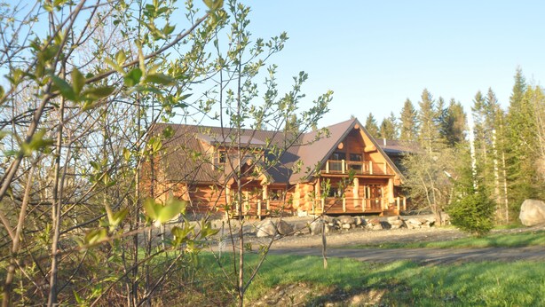 A large log cabin with a prominent front porch, surrounded by trees and a clear sky. - Au domaine de La Giroux-ette (La Patrie)
