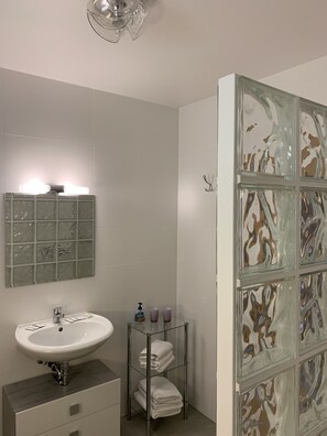 A bathroom with a white sink, a glass shelf with towels, and a decorative glass panel.