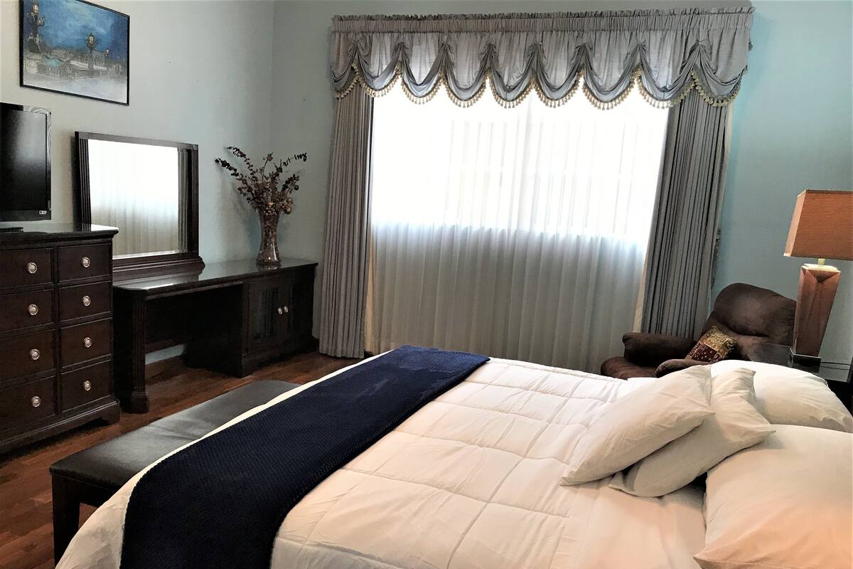Ein Schlafzimmer mit Bett, Schminktisch, Schreibtisch, Stuhl, Lampe und einem Bild an der Wand.