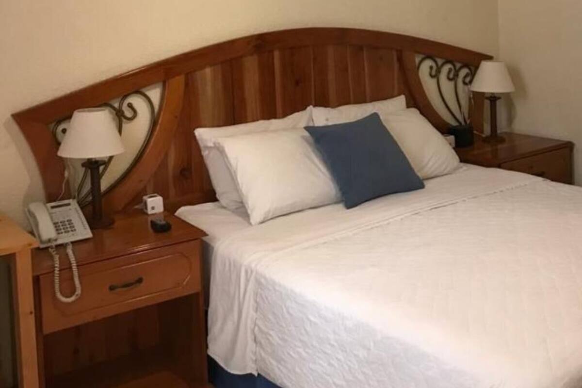 Ein ordentlich bezogenes Bett mit weißen und blauen Kissen, einem Holzkopfstück und Nachttischen mit Lampen.