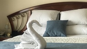 Een keurig opgemaakt bed met een handdoek in de vorm van een zwaan, een blauw kussen en een wit kussen op een houten hoofdbord.
