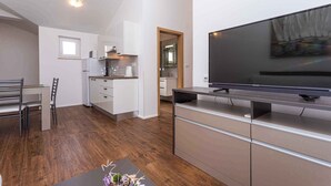 A modern apartment with a dining area, kitchenette, and a large flat-screen TV.