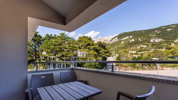 A balcony with a table and chairs, overlooking a mountainous landscape with trees and buildings.