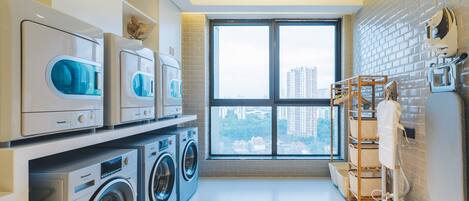 A modern laundry room with stacked washing machines, a drying rack, and a large window offering a city view.