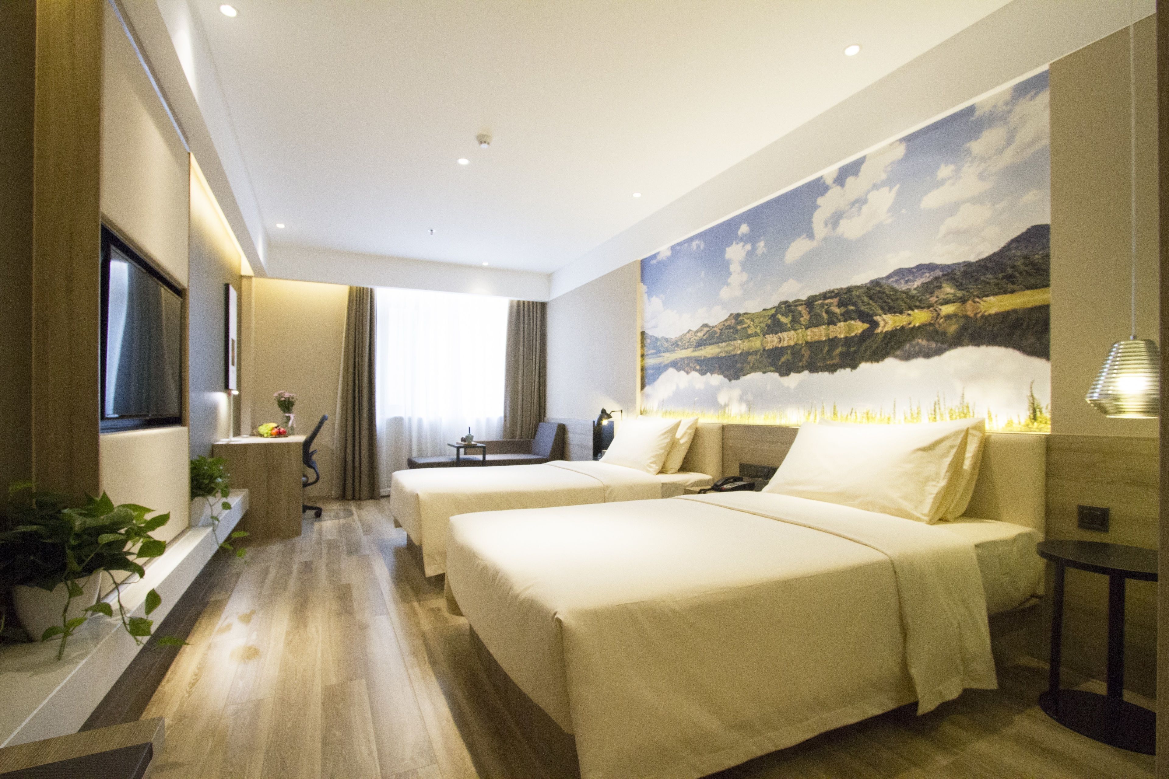 A hotel room with two beds, a desk, a chair, a small table, and a large window.