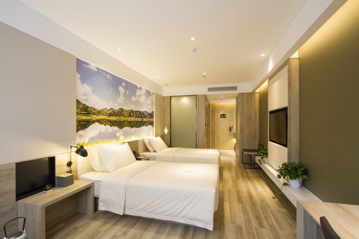 Ett modernt hotellrum med två sängar, en platt-TV, ett skrivbord och en stor landskapsmålning på väggen.